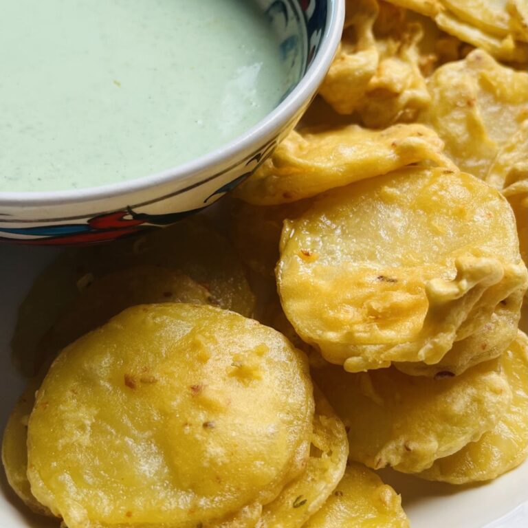 Close-up of crispy fried potato slices next to a bowl of creamy green dip. The potatoes are golden and slightly textured, while the dip is smooth with a light green color, placed on a decorative bowl.
